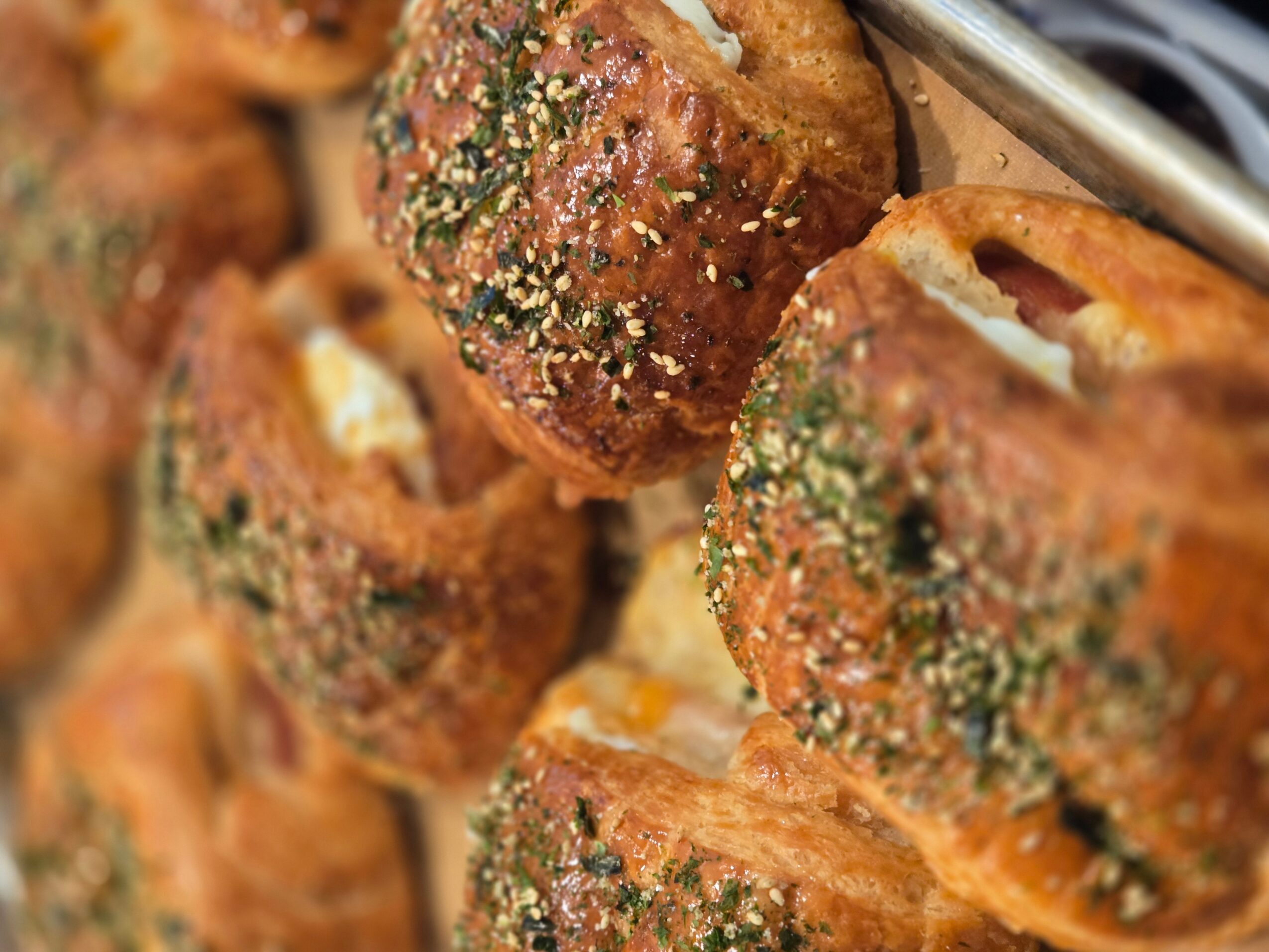 Close-up of baked bread rolls sprinkled with herbs and sesame seeds, some with cheese filling visible.