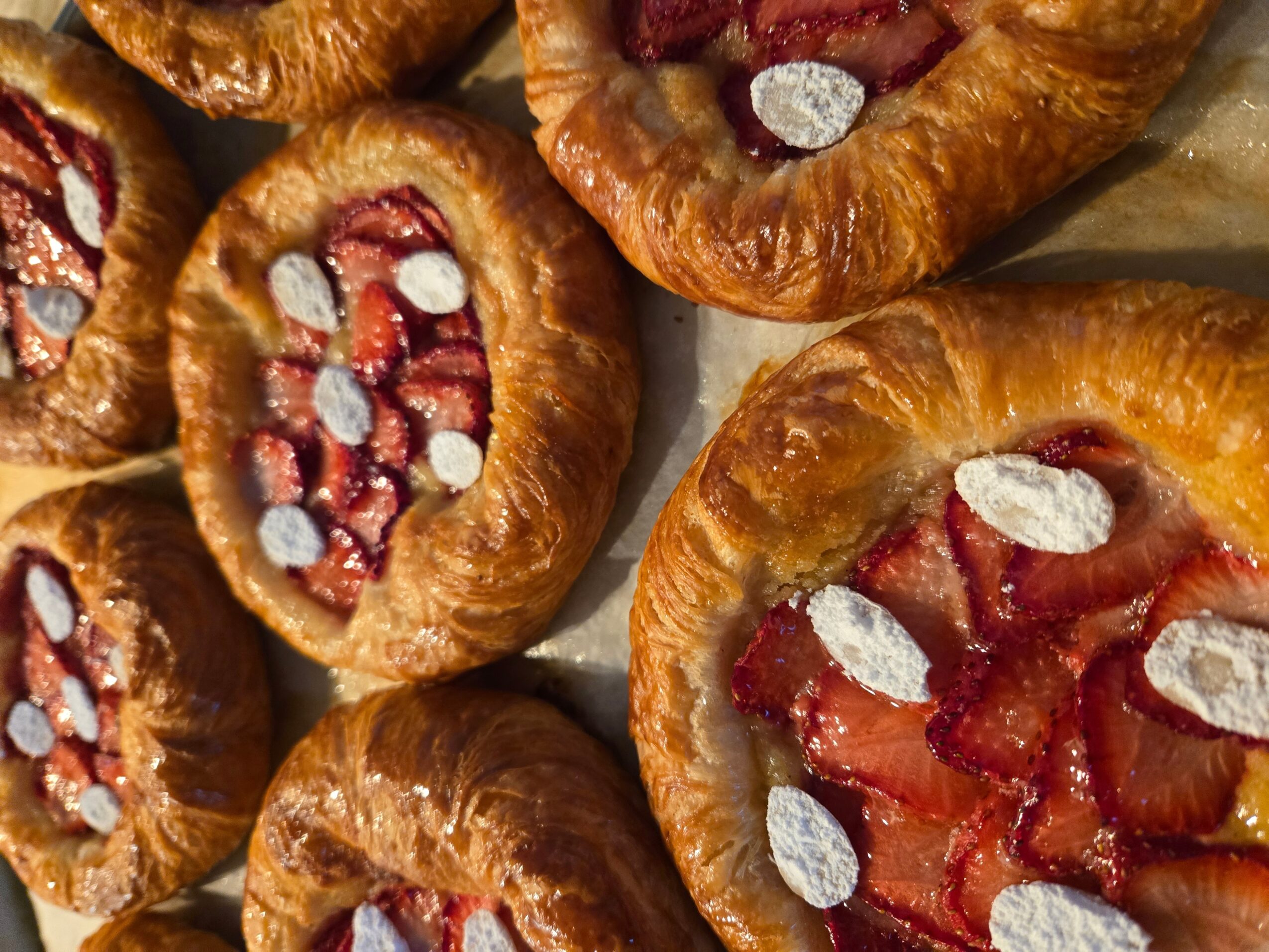 Close-up of baked pastries filled with strawberries and topped with almond slices, arranged on a tray.