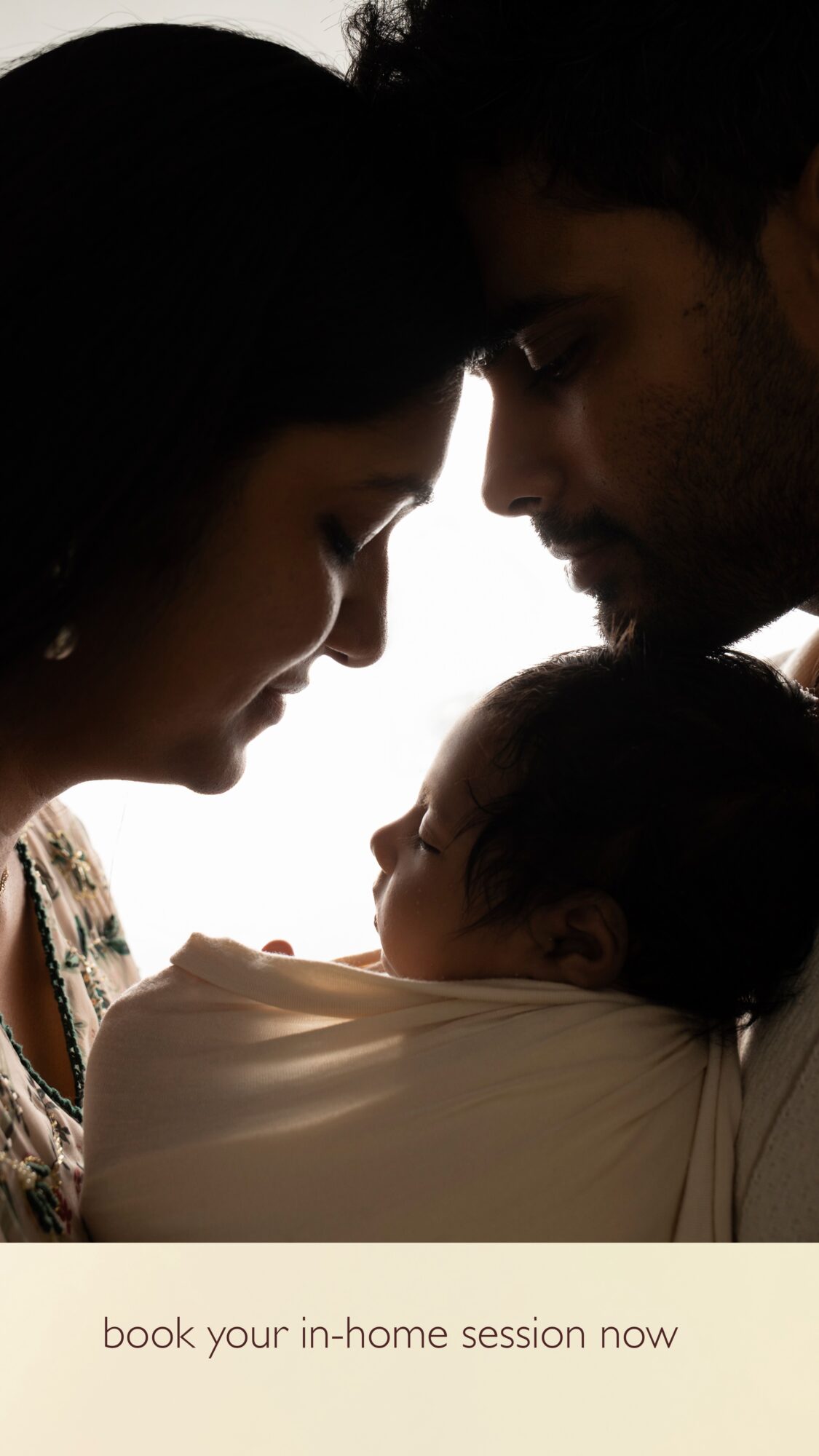A family with a woman, man, and baby face each other closely, with the baby wrapped in a blanket.