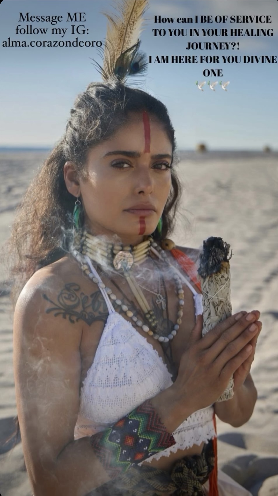 Woman with traditional jewelry and markings on her face holds a small object, standing outdoors with a clear sky.