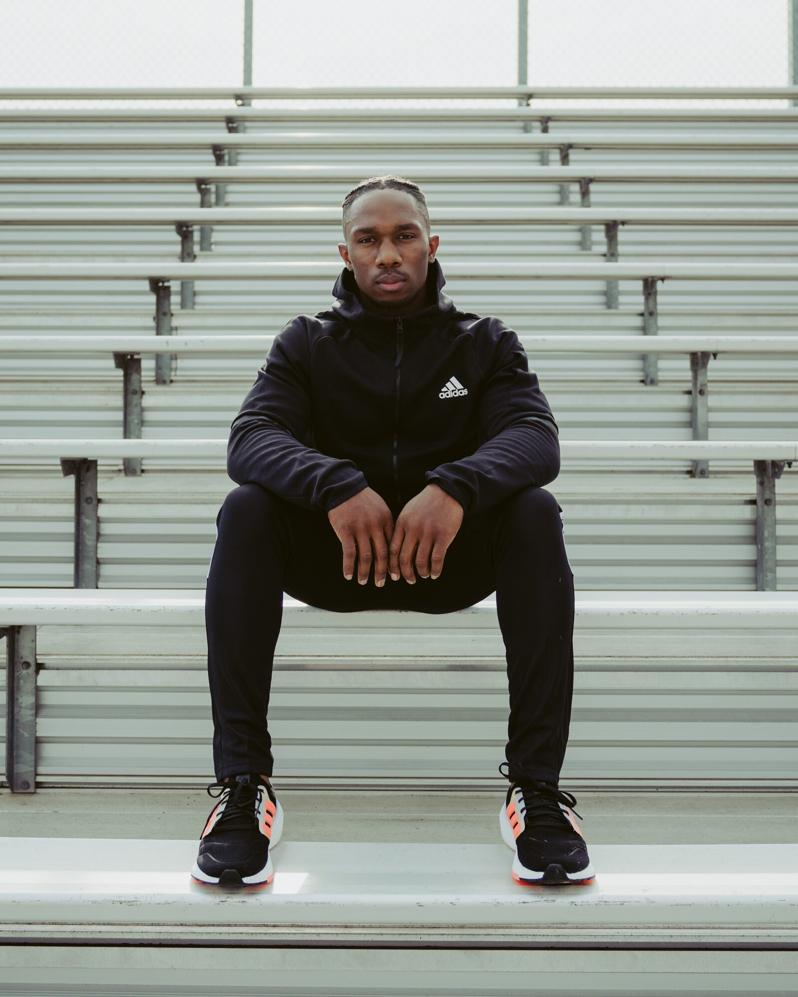 Man sitting on bleachers in athletic clothing, arms resting on knees, looking at camera.