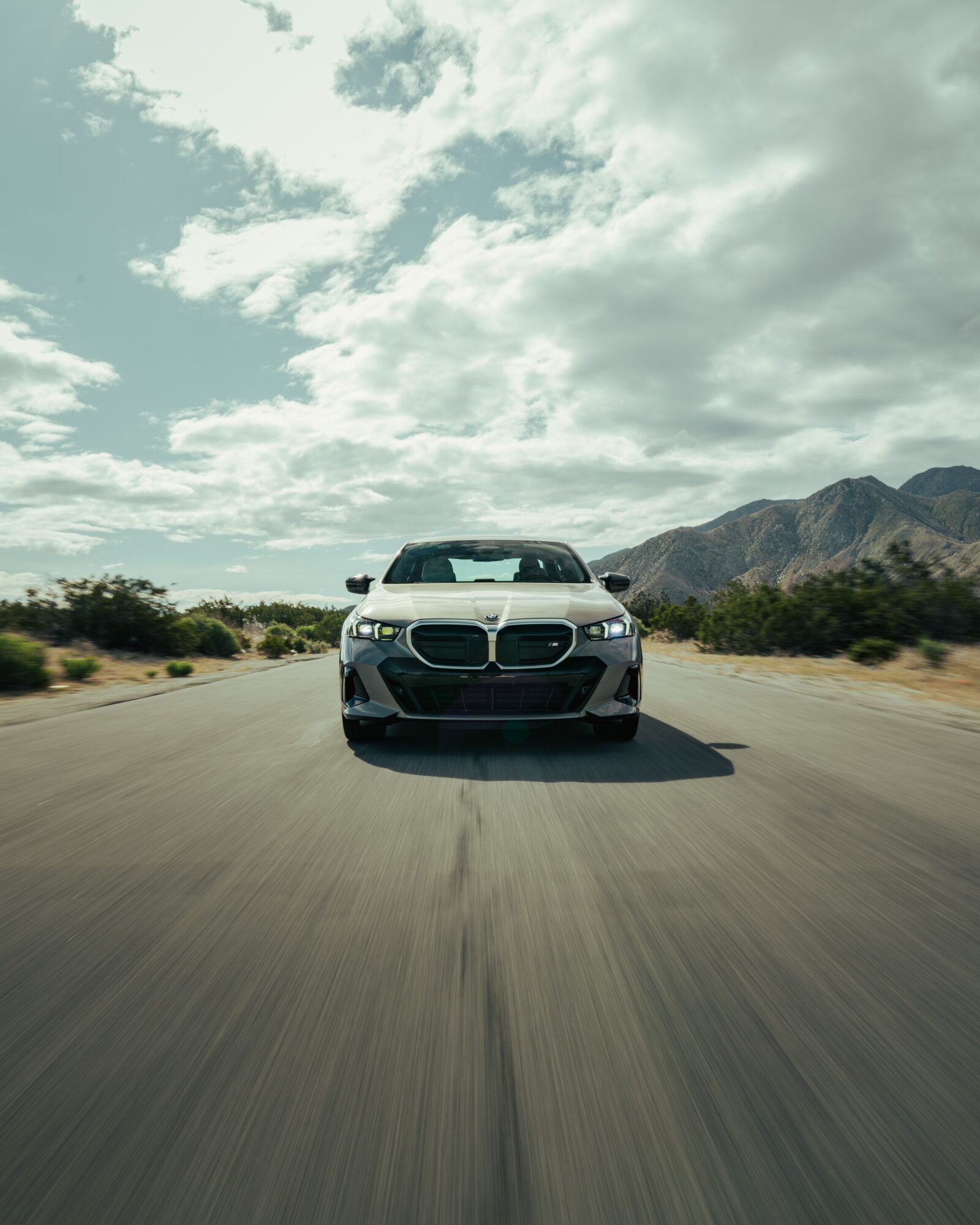 White car driving on a desert road with mountains and cloudy sky in the background.