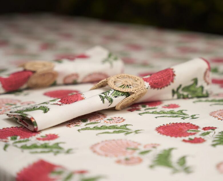 Tablecloth with red and pink floral pattern, partially rolled napkin with a decorative button, on a table.
