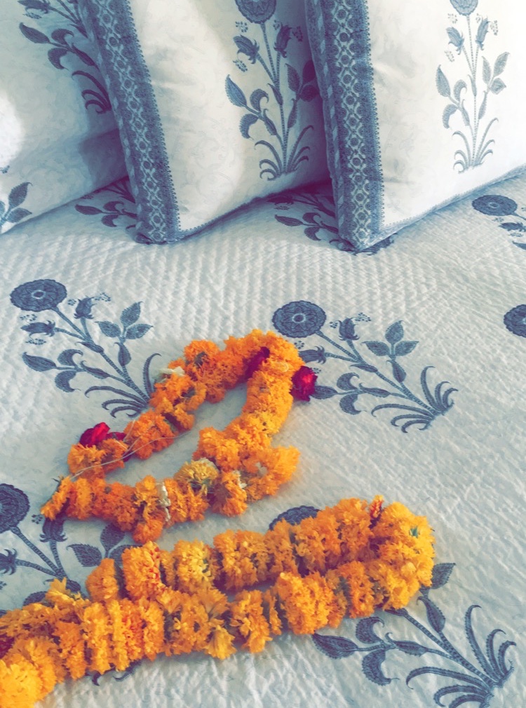 Two orange marigold flower garlands on a patterned bedspread with pillows in the background.