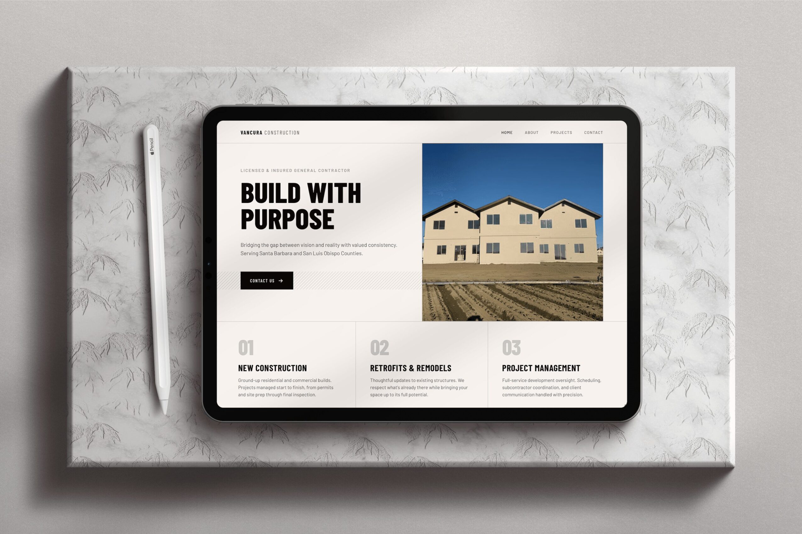 Tablet displaying a website with a house image and text, placed on a marble surface with a stylus nearby.