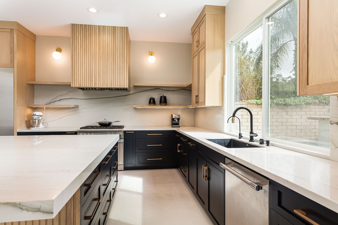 Modern kitchen with white countertops, black lower cabinets, wooden upper cabinets, and a large window with outdoor view.