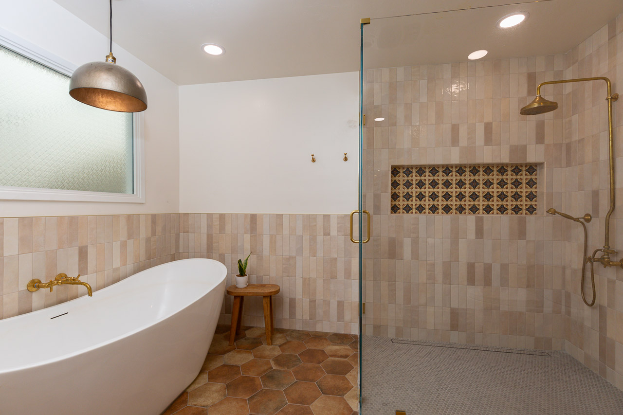 Bathroom with a freestanding bathtub, small stool, and a walk-in shower with beige tiles and a decorative niche.