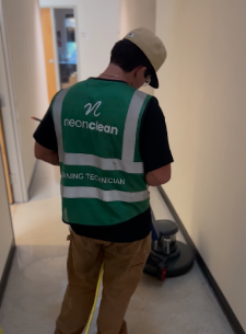 Person in a green vest and beige cap operating cleaning equipment in a hallway.