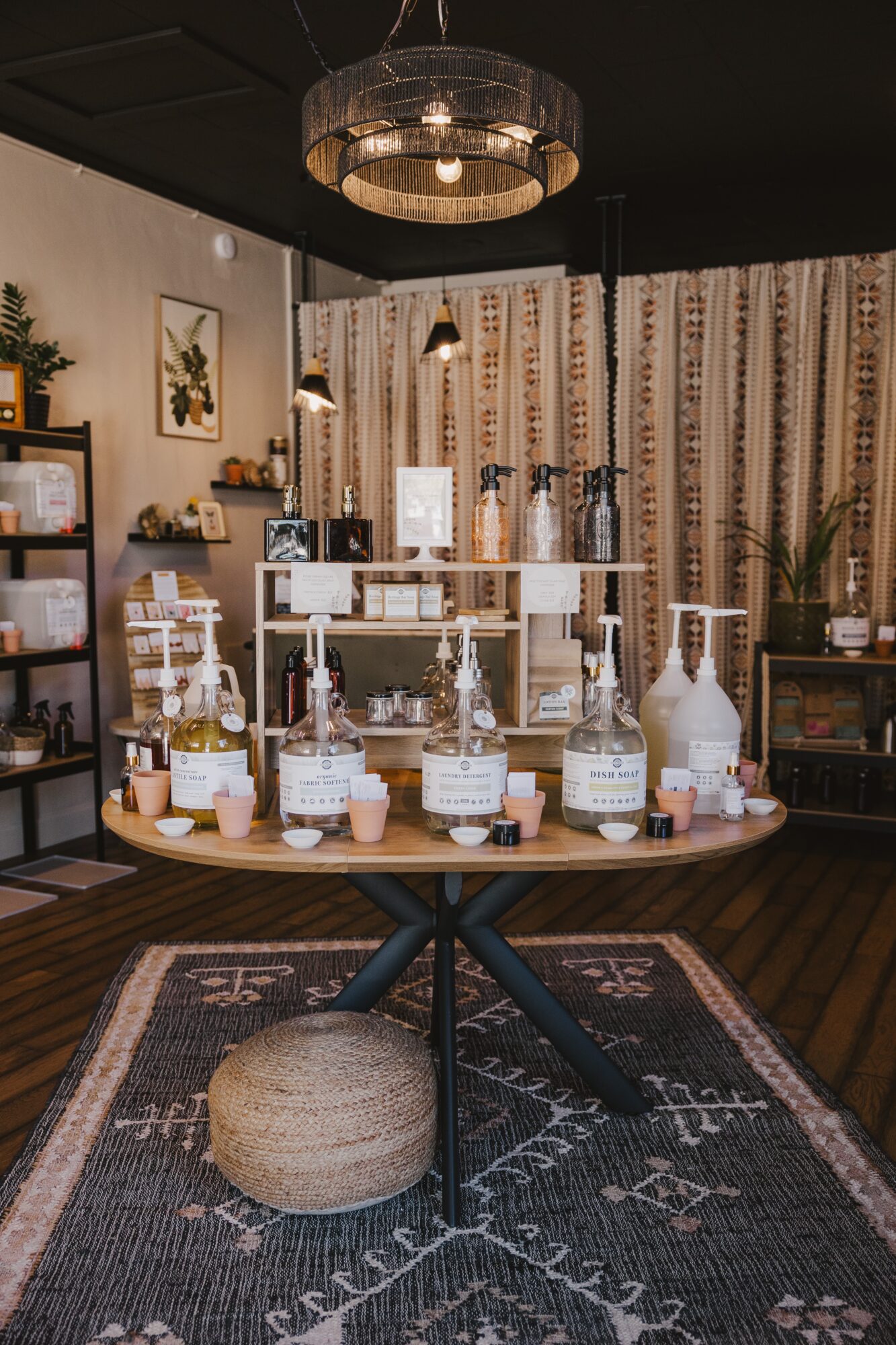 Display of various bottles and jars on a round table in a cozy room with patterned curtains and decorative items.
