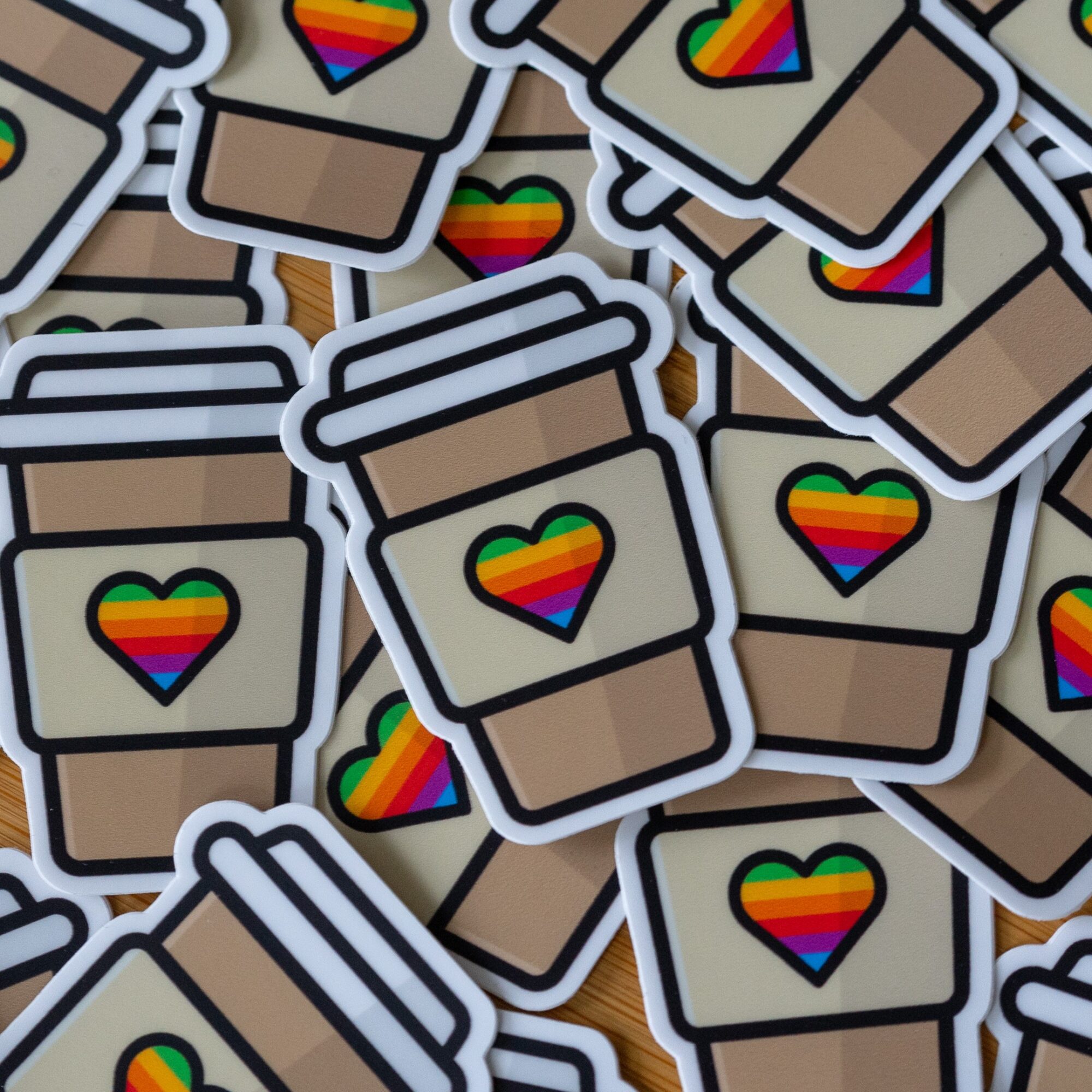 Multiple coffee cup stickers with rainbow heart logos overlapping each other.