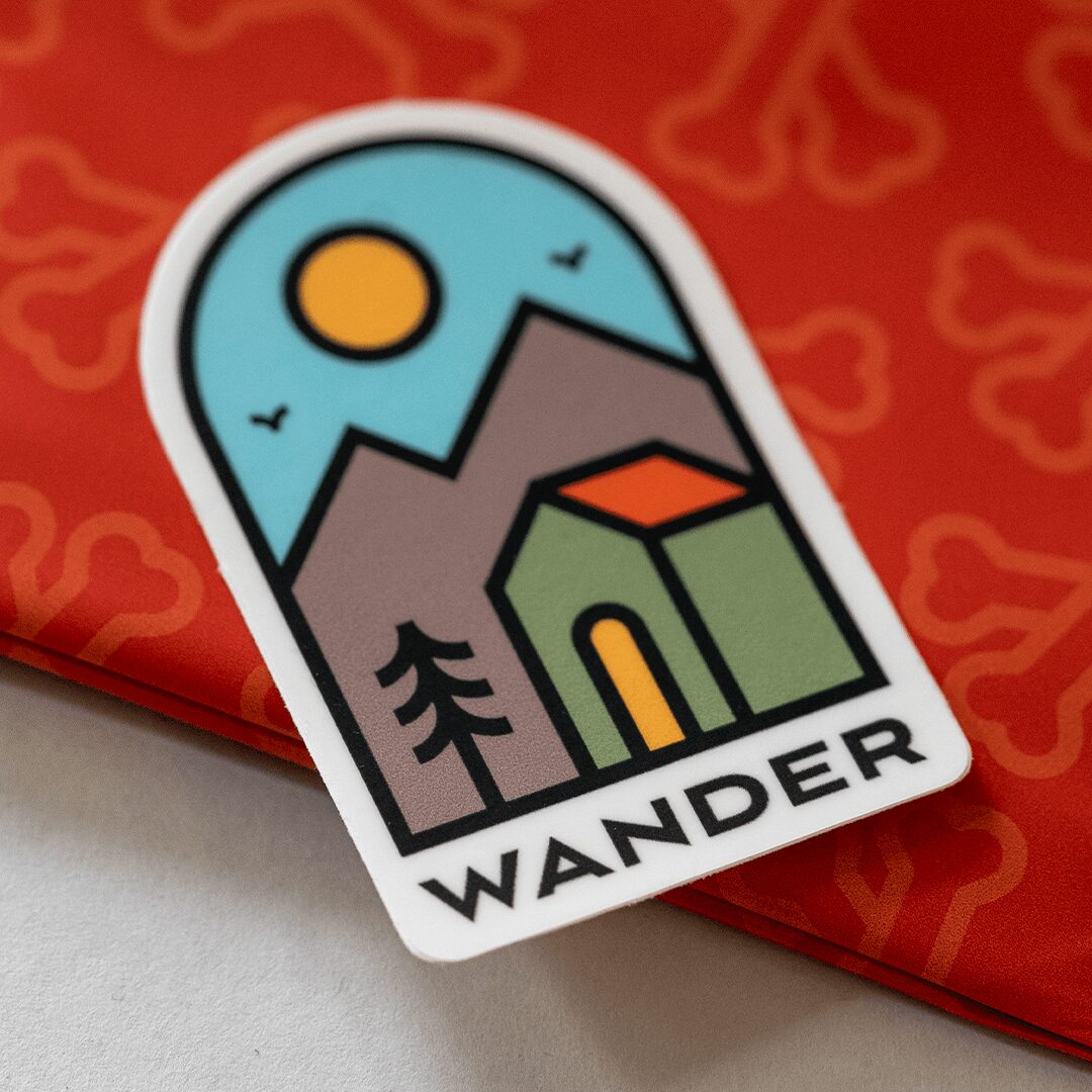 Sticker with a mountain, tree, sun, and birds, labeled 'WANDER', on red background.
