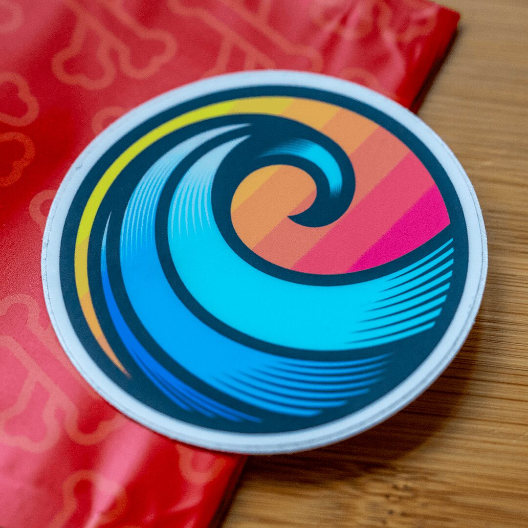 Colorful circular logo with wave design on a wooden surface with red fabric nearby.