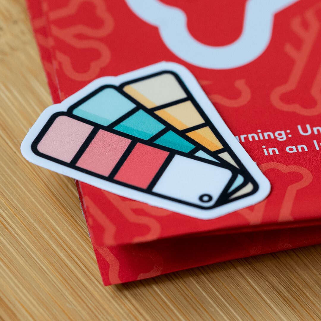 Colorful sticker with geometric shapes on a red background, placed on a wooden surface.