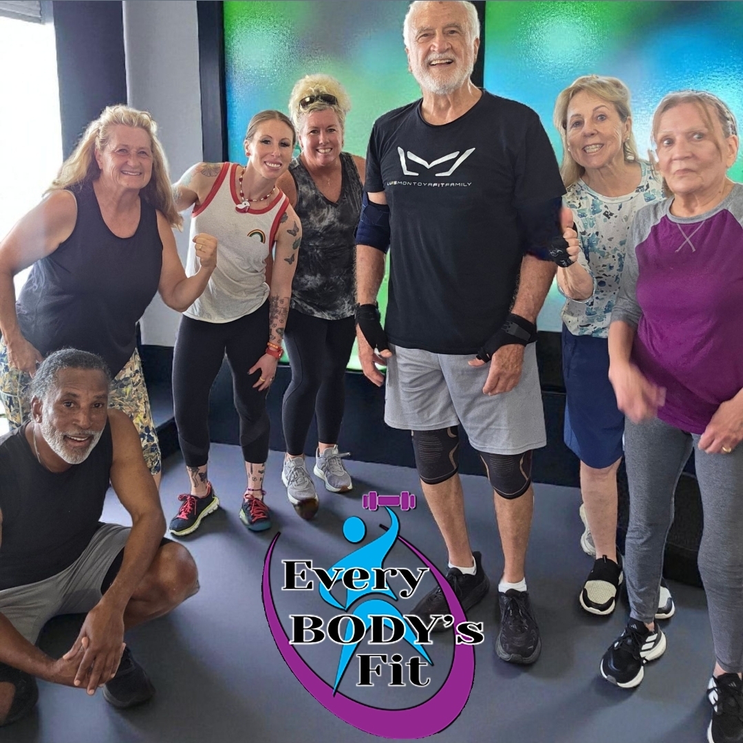 Group of seven diverse people in workout clothes smiling in a fitness studio with a logo that says 'Every Body's Fit'.