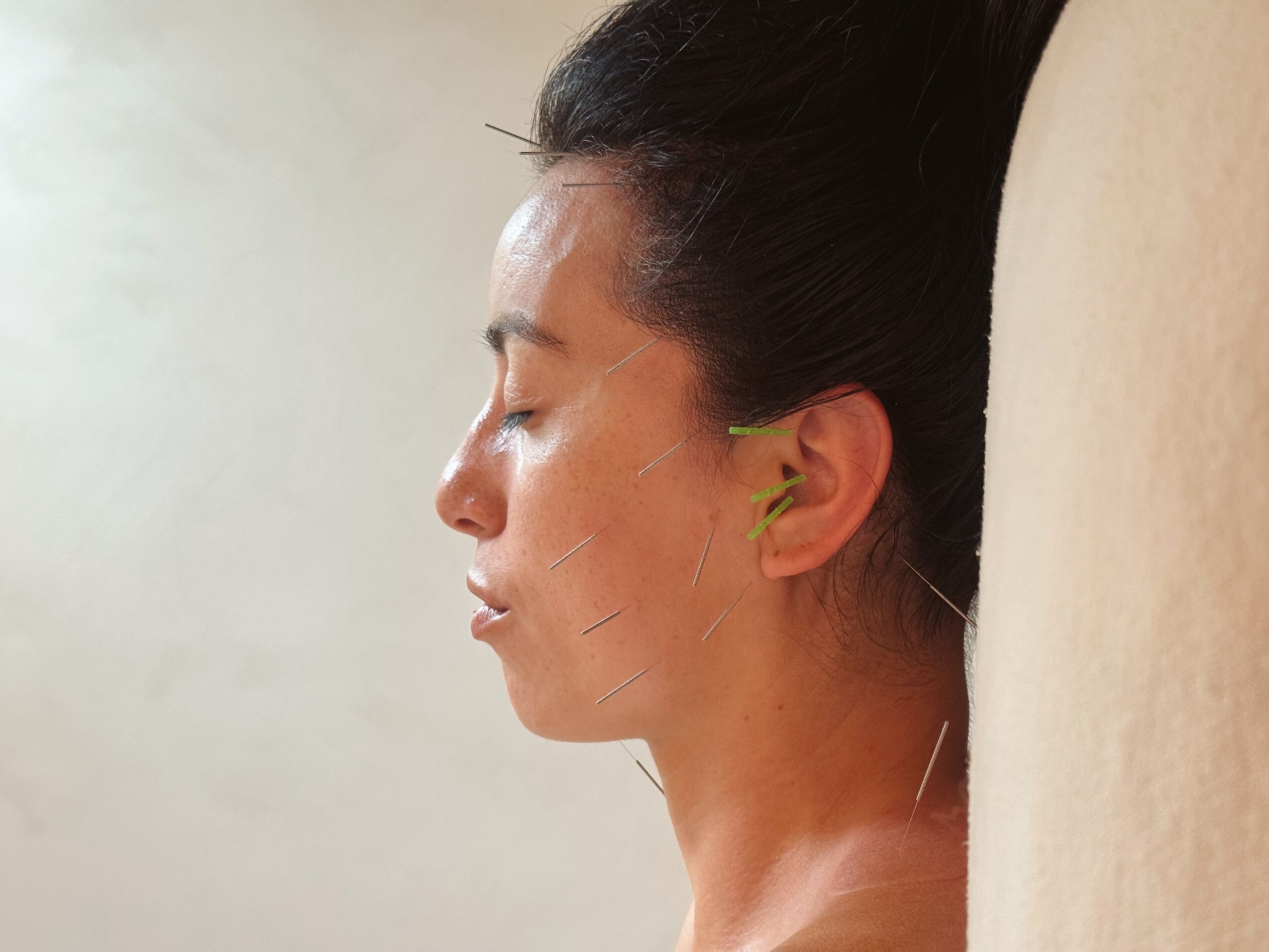 Side profile of a woman with dark hair tied back, leaning against a wall with her eyes closed.