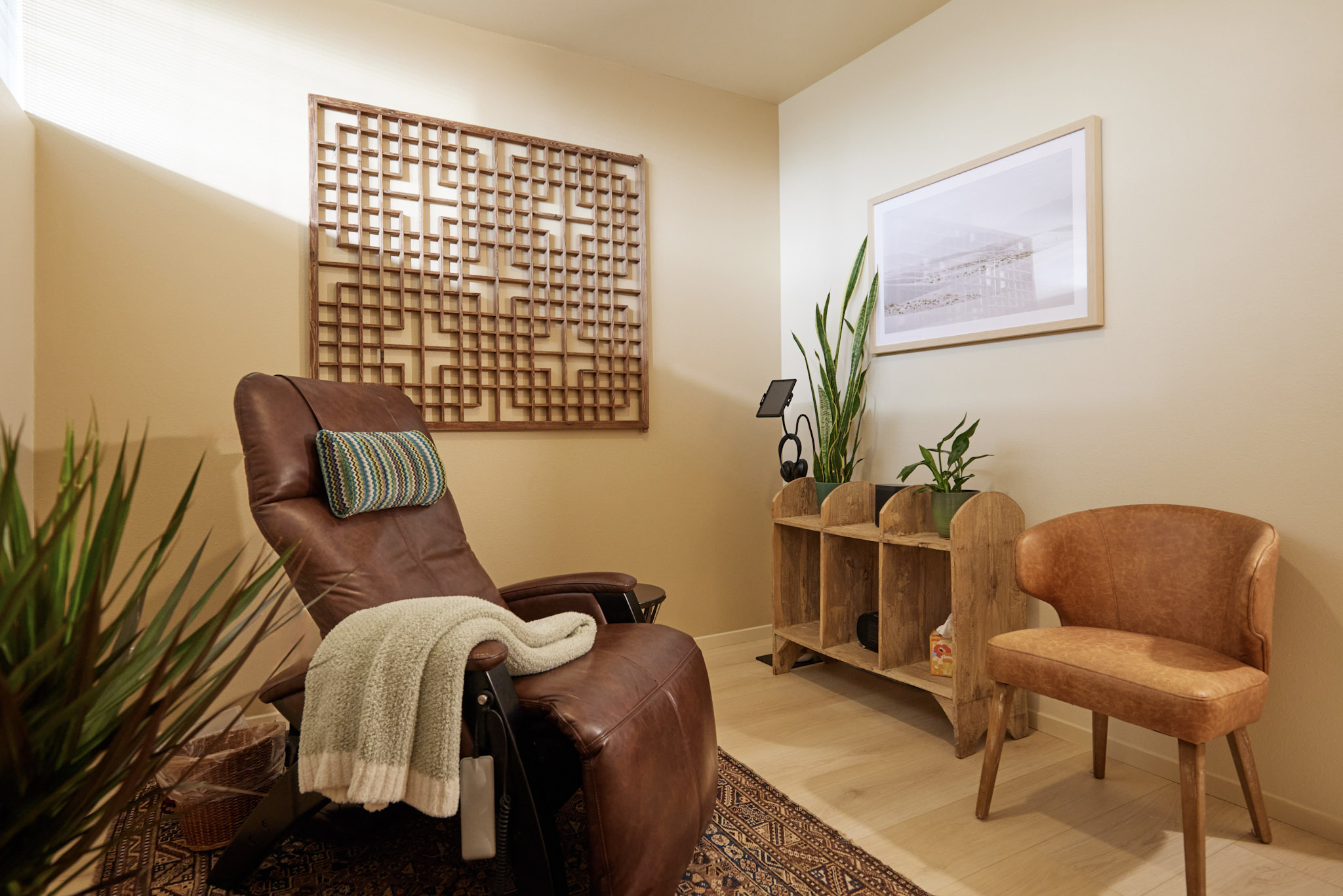 Cozy room with a brown recliner, wooden side table, and a peach-colored chair, decorated with plants and wall art.