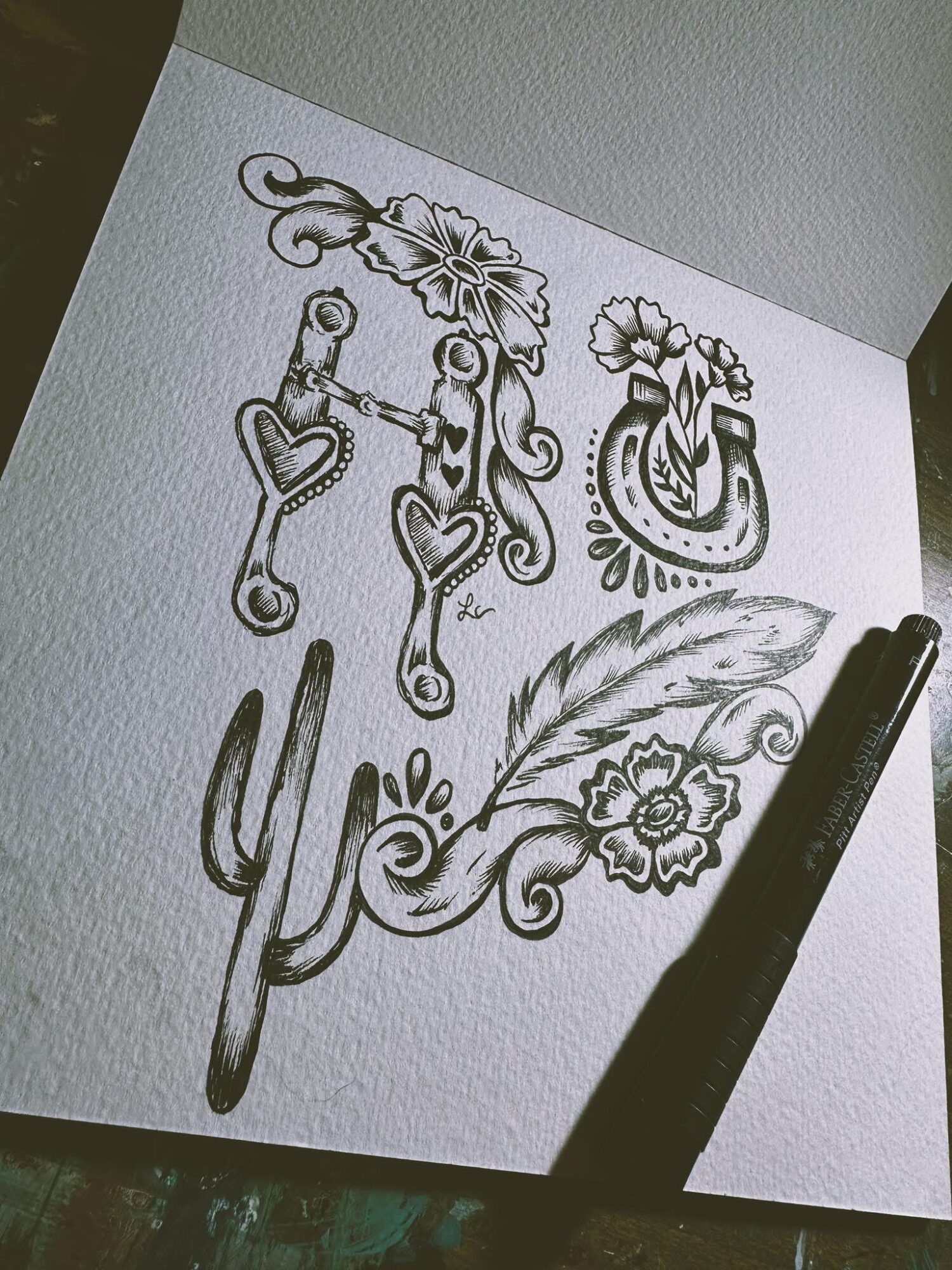 Sketch of floral and heart designs on paper with a pen nearby, viewed from an angle.