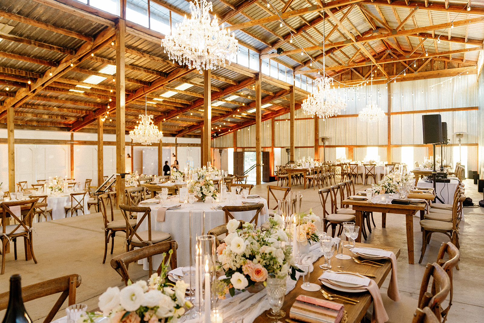 Elegant event space with chandeliers, wooden chairs, and tables decorated with flowers and tableware.