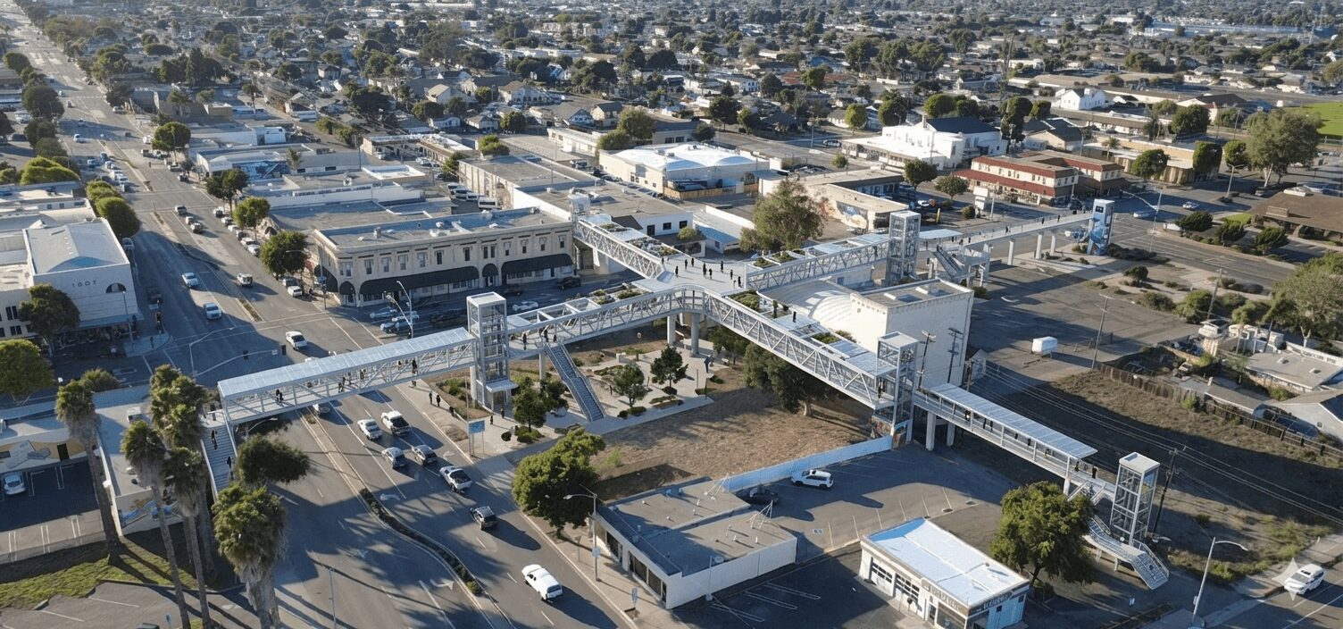 Aerial view of a city street with buildings, trees, and a pedestrian bridge over the road.