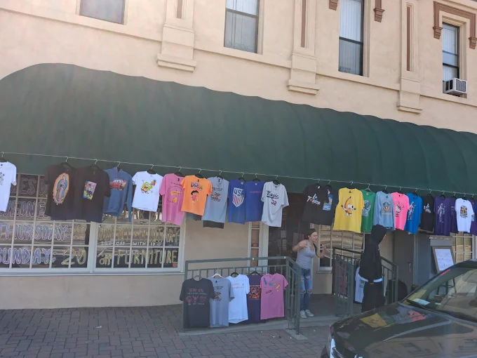 Clothes hanging on a line outside a building with windows and a green awning, people browsing, parked car nearby.