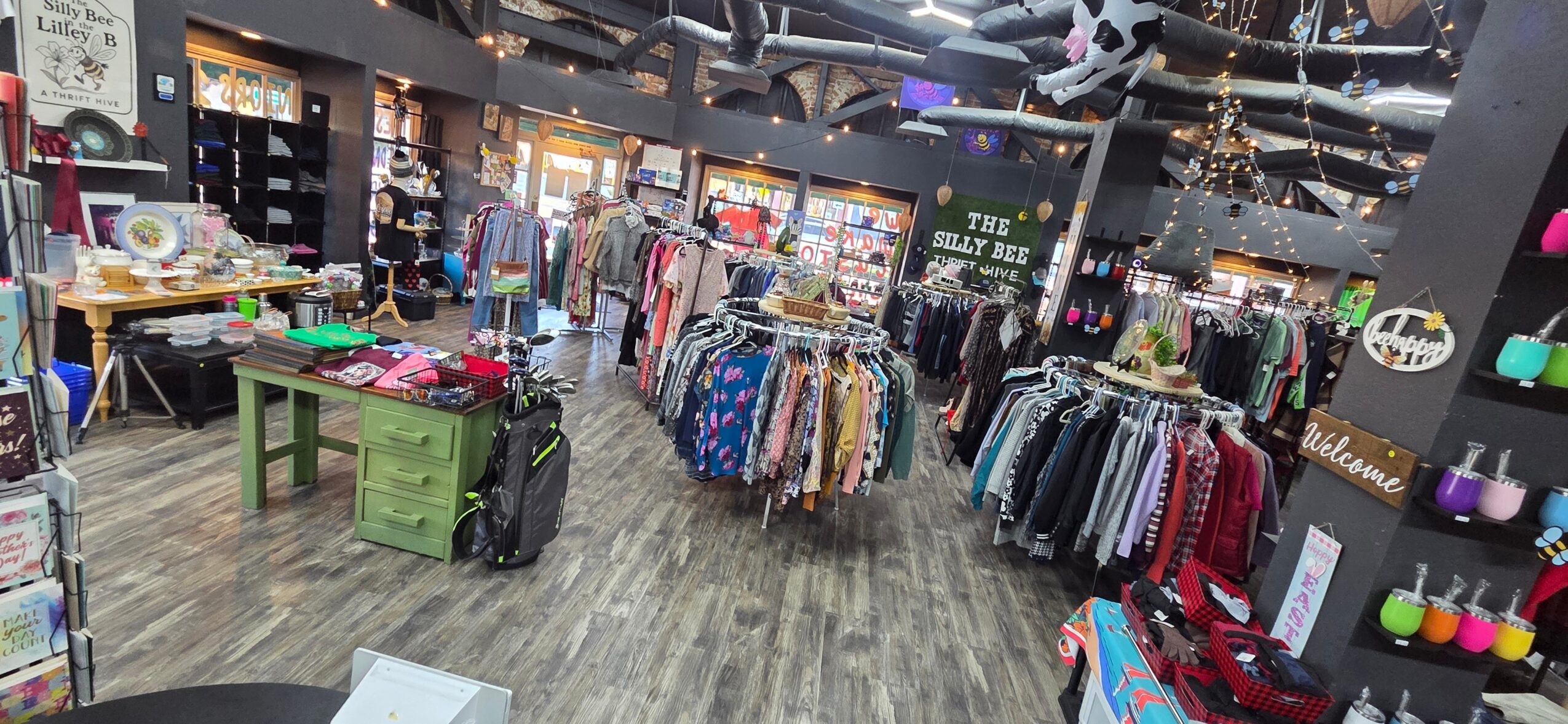Clothing store with racks of clothes, shelves, and shopping bags, and a wooden floor, viewed from the front.