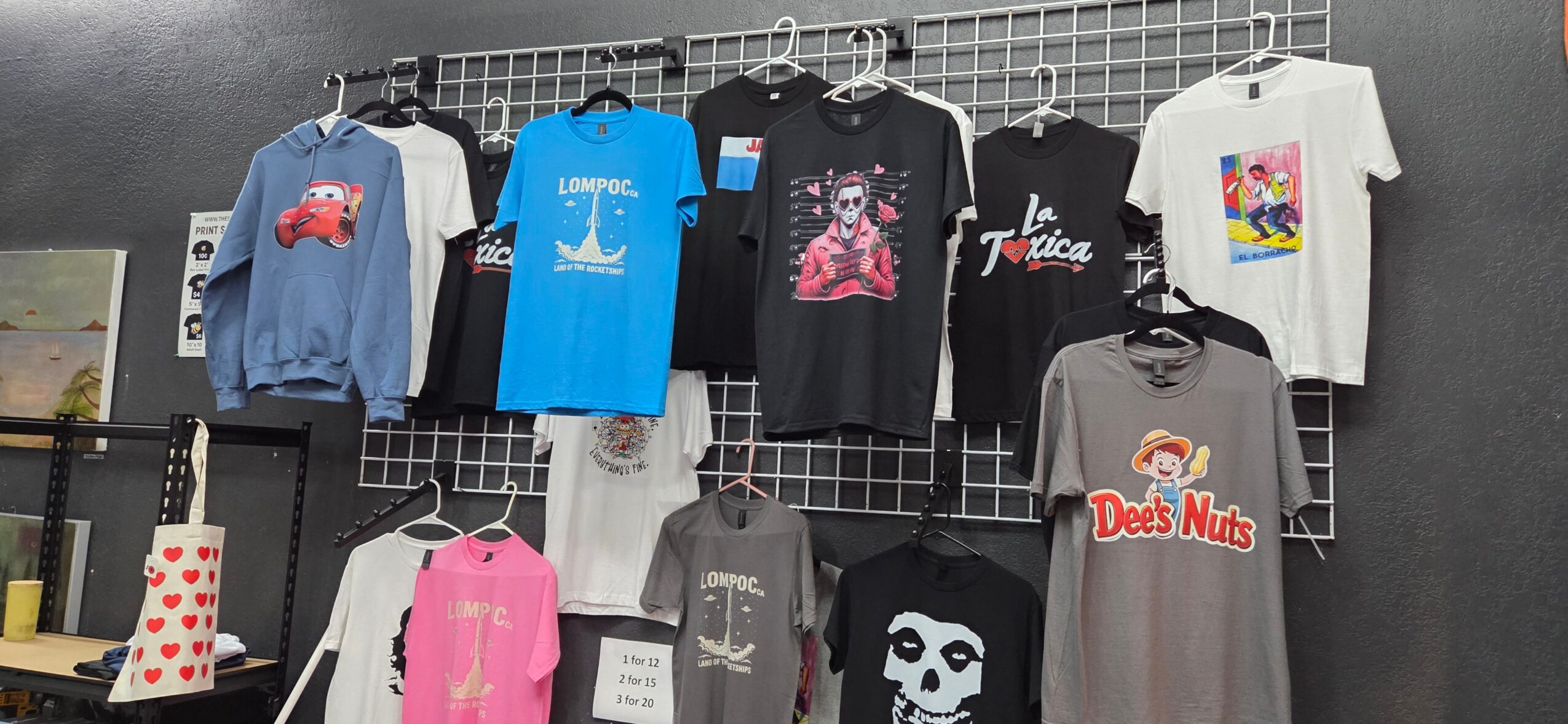 Display of various T-shirts hanging on a wall, some with graphic designs and logos, in a retail setting.