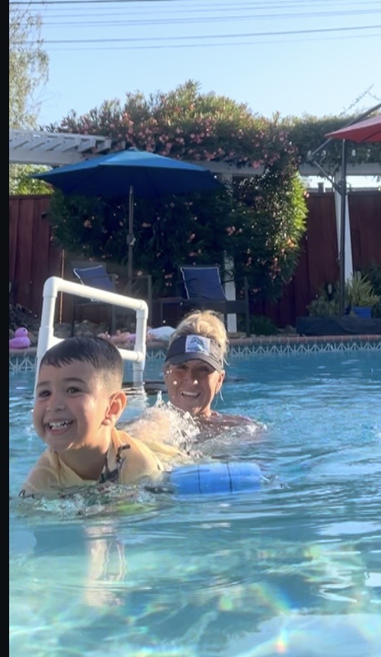 Three children swimming in a pool with umbrellas and trees in the background.
