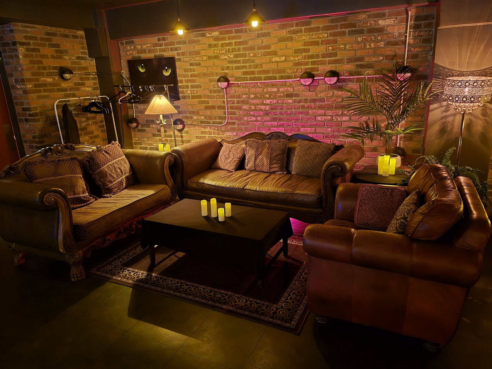 Cozy living room with leather sofas, a coffee table, candles, a lamp, and a brick wall with pink lighting.