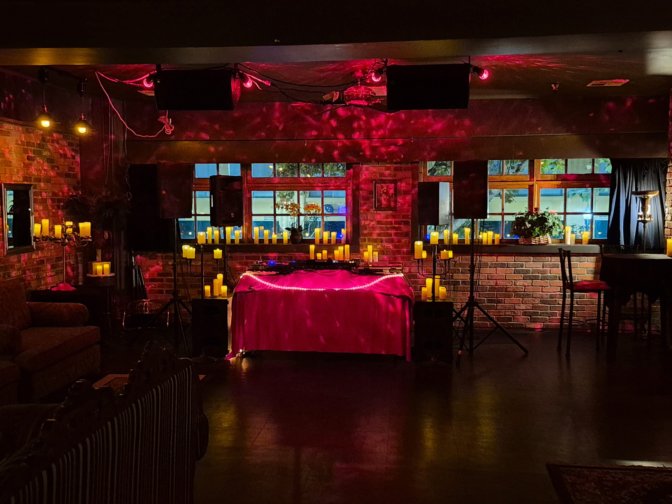 Indoor venue with a table covered in a pink cloth, surrounded by candles, with windows and brick walls in the background.