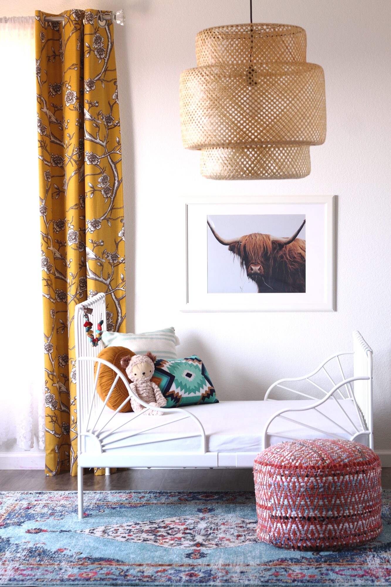 Living room with yellow patterned curtains, white sofa, framed animal photo, woven pendant light, and pink pouf.