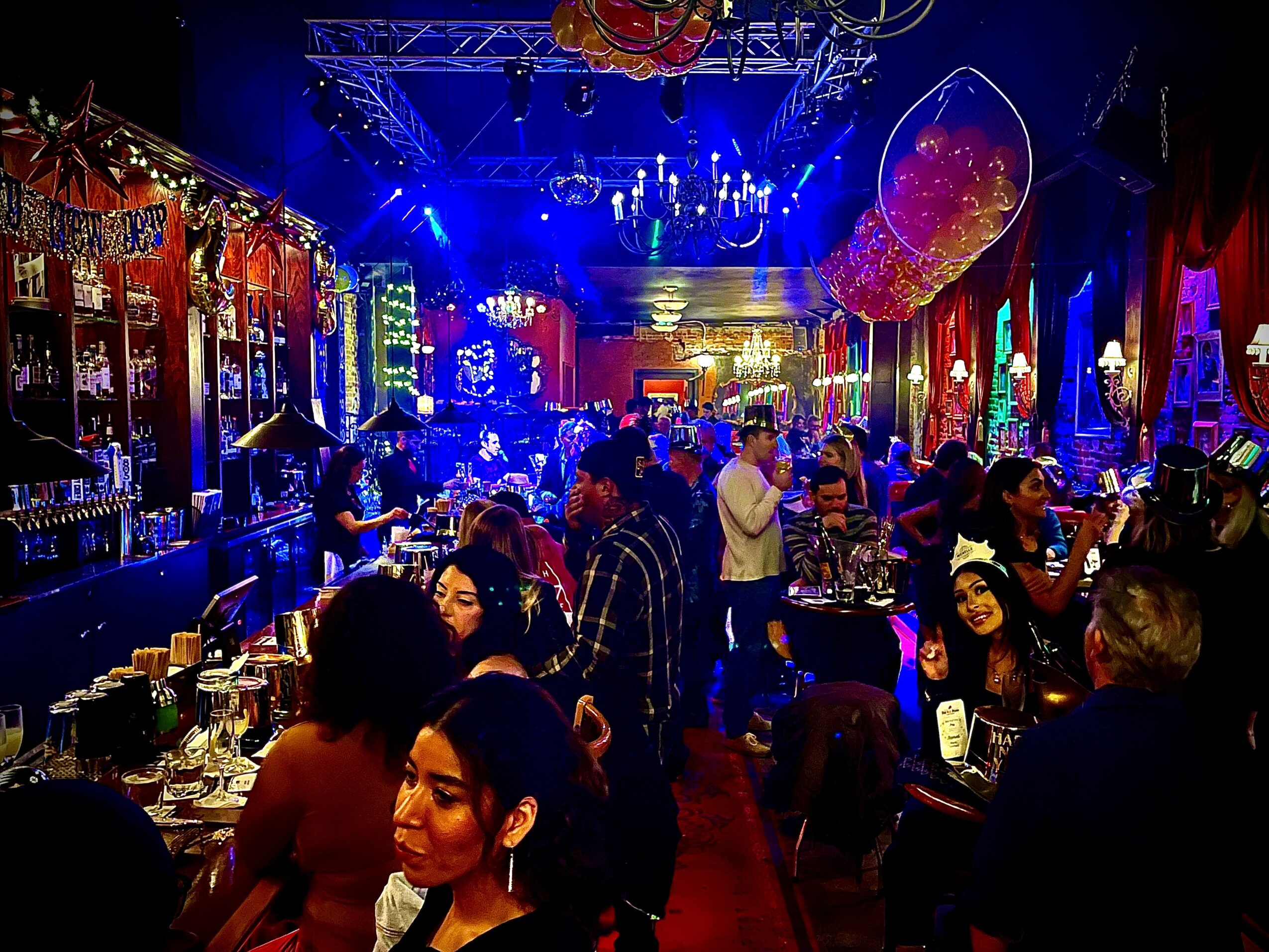 Crowded bar or nightclub with colorful lighting, decorations, and people socializing and enjoying drinks.