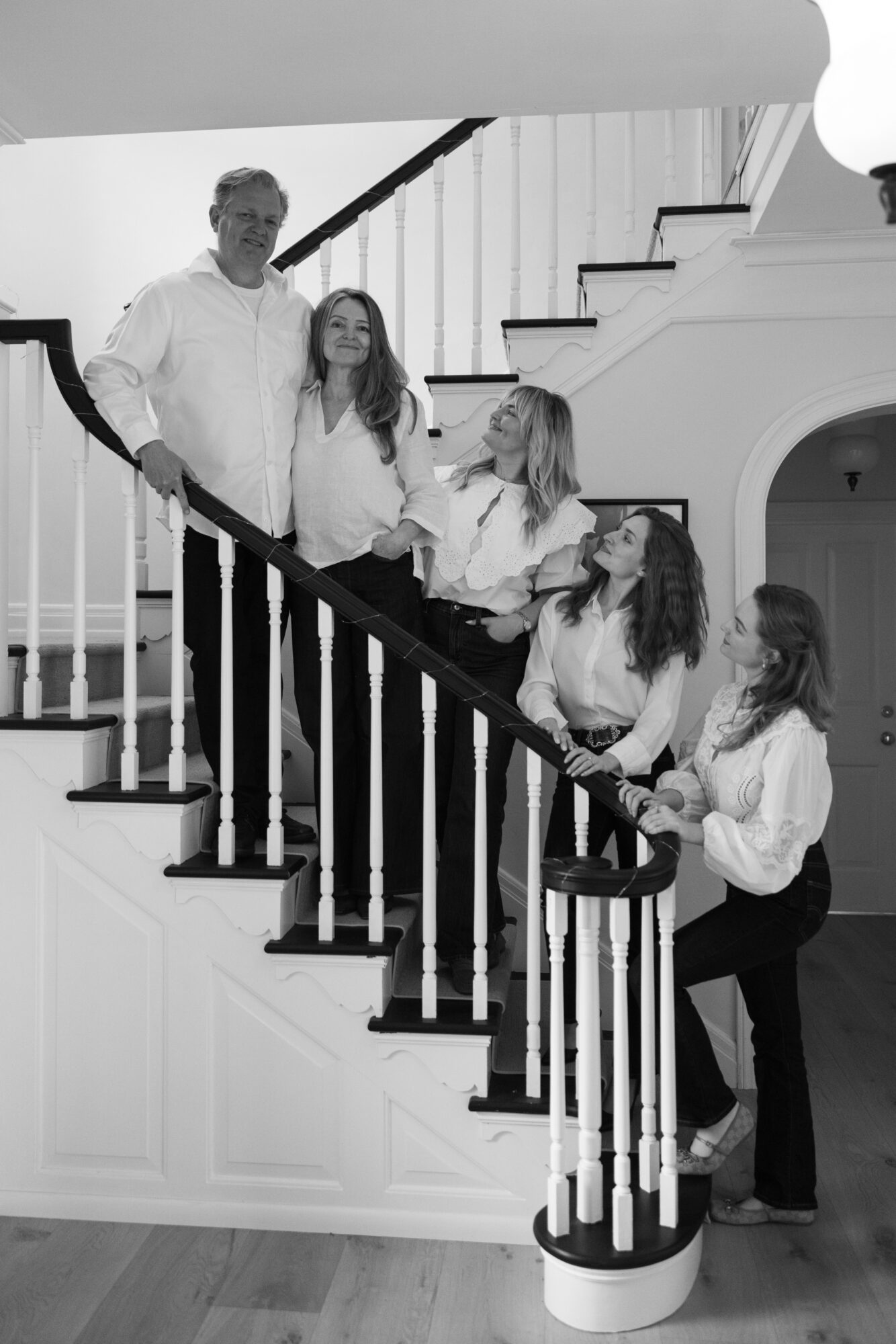 Six people, including children and an adult, pose on a staircase inside a house, smiling and looking at the camera.