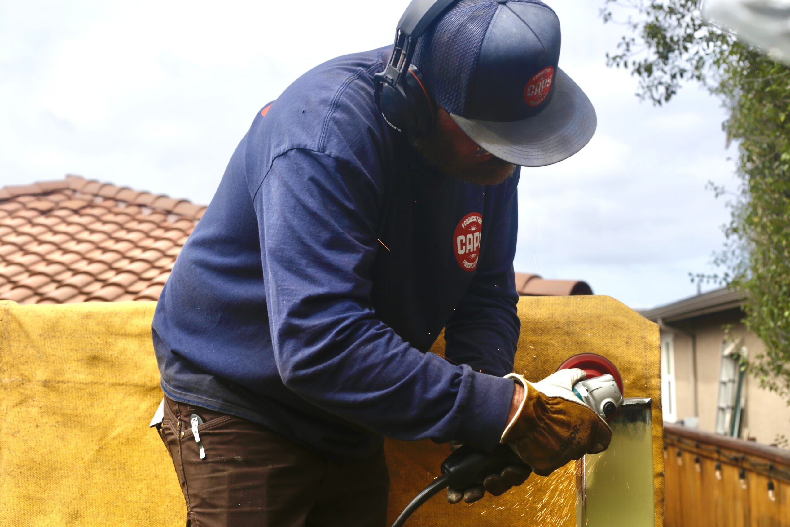 Person wearing a dark cap, navy jacket, and gloves, working outdoors with a yellow surface and trees in background.
