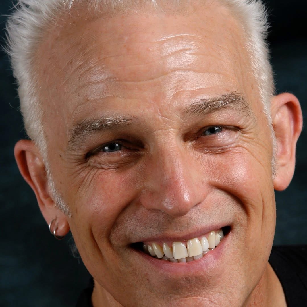 Close-up of smiling older man with white hair, earrings, and visible teeth.