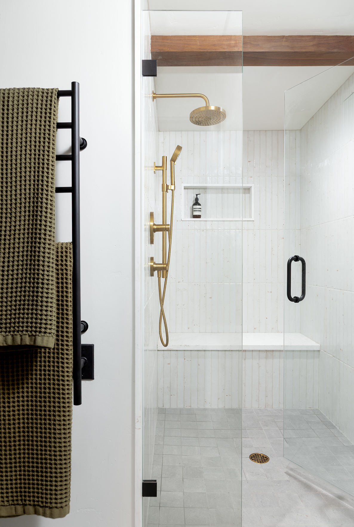 Shower area with gold fixtures, a built-in shelf, and a glass door, viewed from the side with a towel rack nearby.