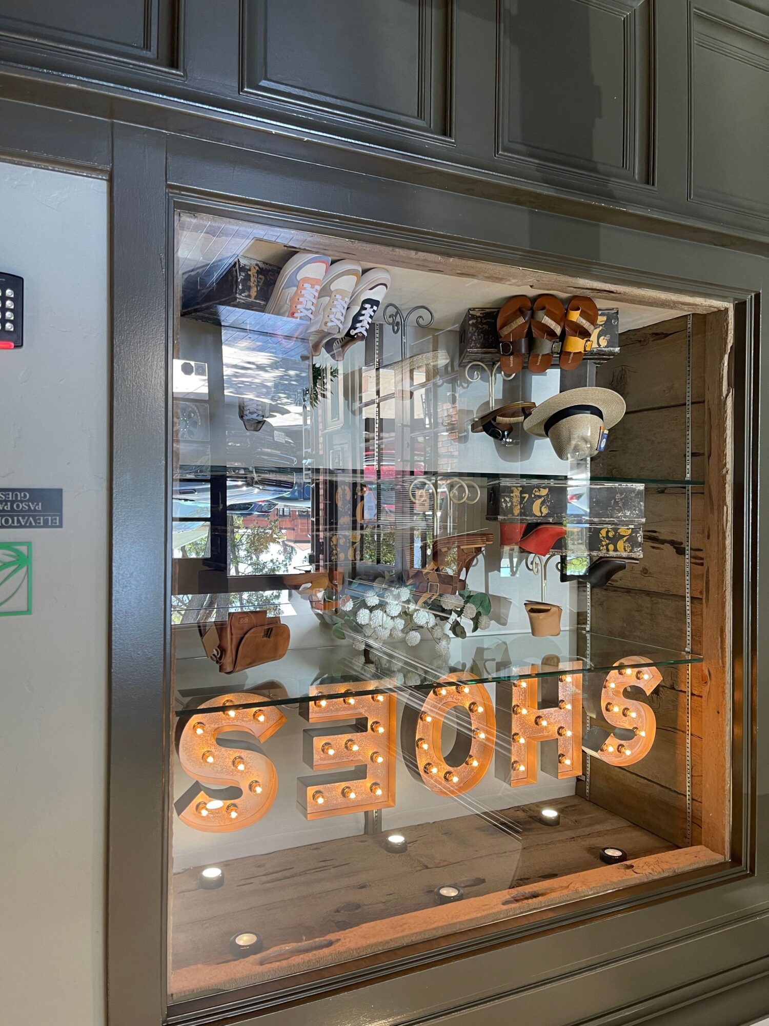 View through a glass window showing a store interior with large illuminated letters spelling 'SHOES' and various items inside.