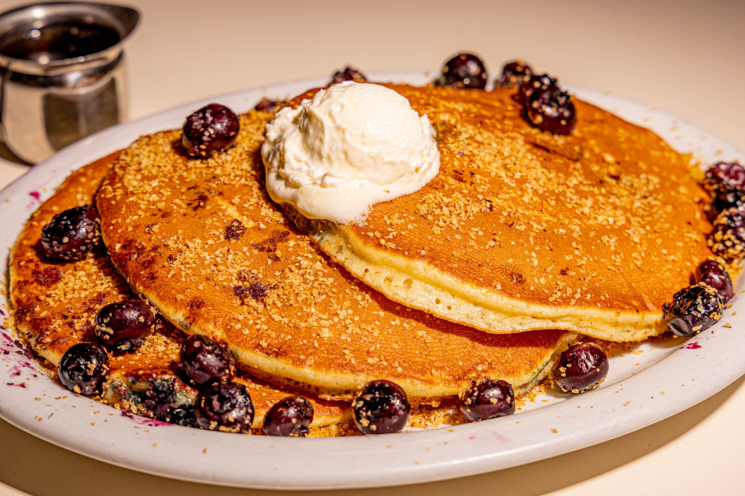 Stack of pancakes topped with butter, surrounded by blueberries on a white plate.