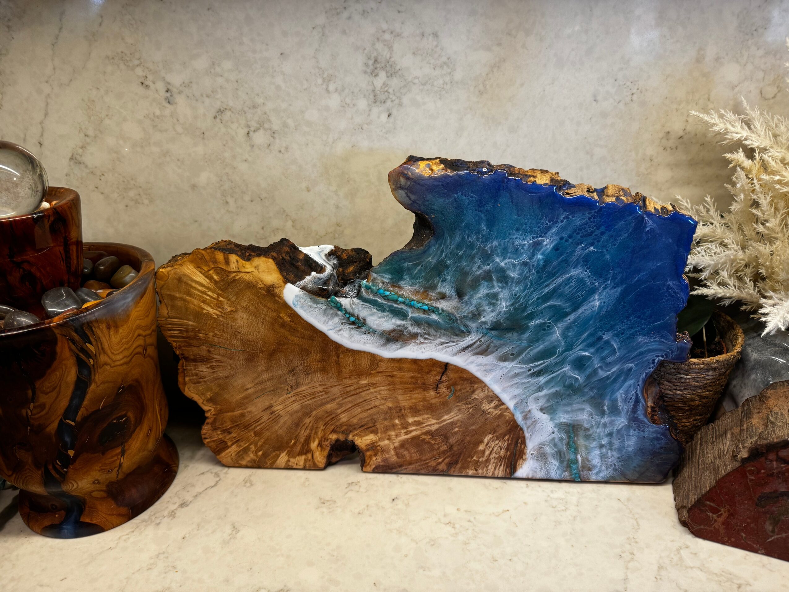 Decorative wooden and resin art piece resembling ocean waves, with surrounding natural elements, on a light-colored surface.