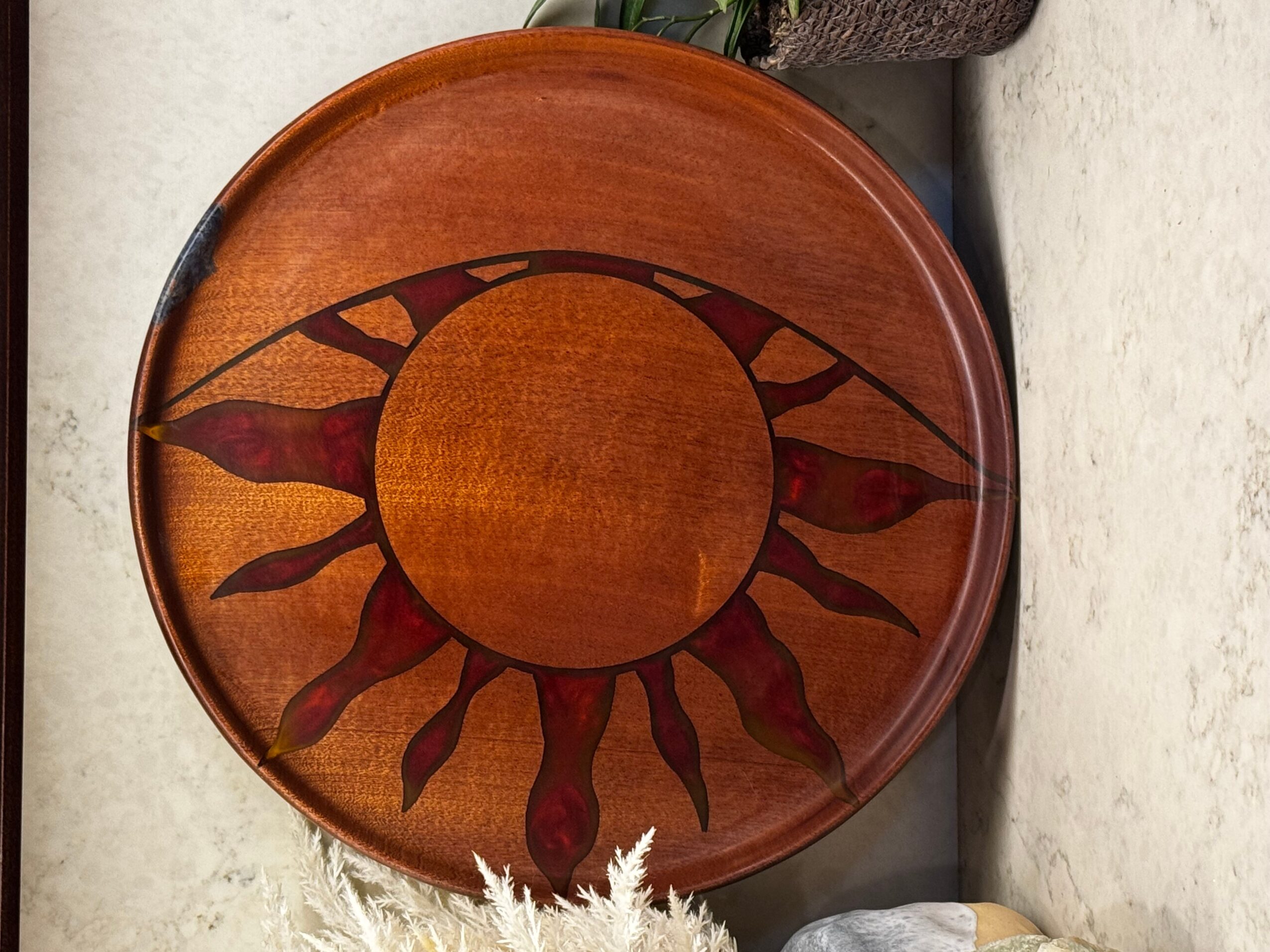 Round wooden decorative plate with a sun design, featuring a central circle and radiating sun rays, on a light surface.