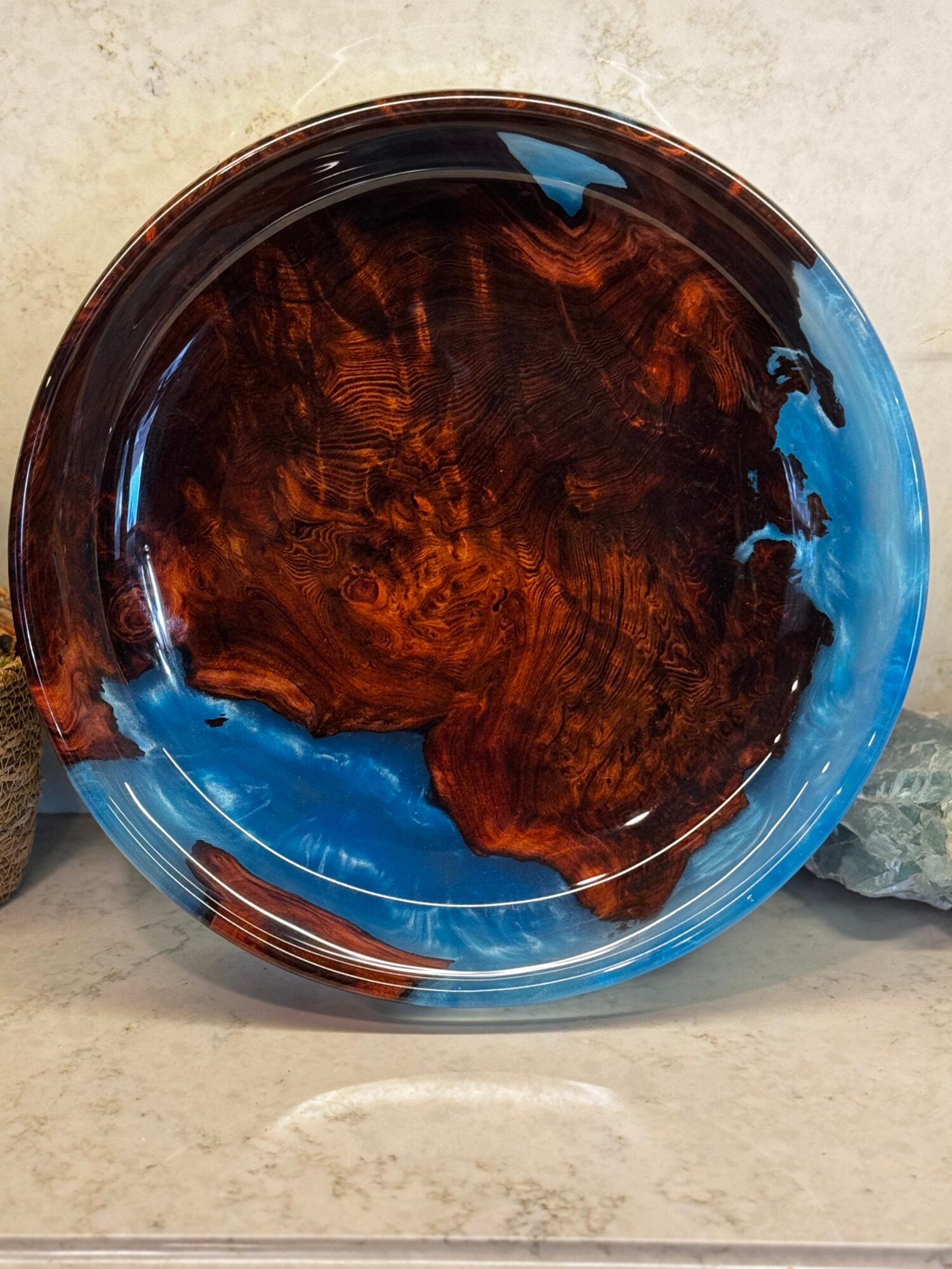 Round decorative plate with brown wood grain pattern and blue accents, placed on a light-colored surface.
