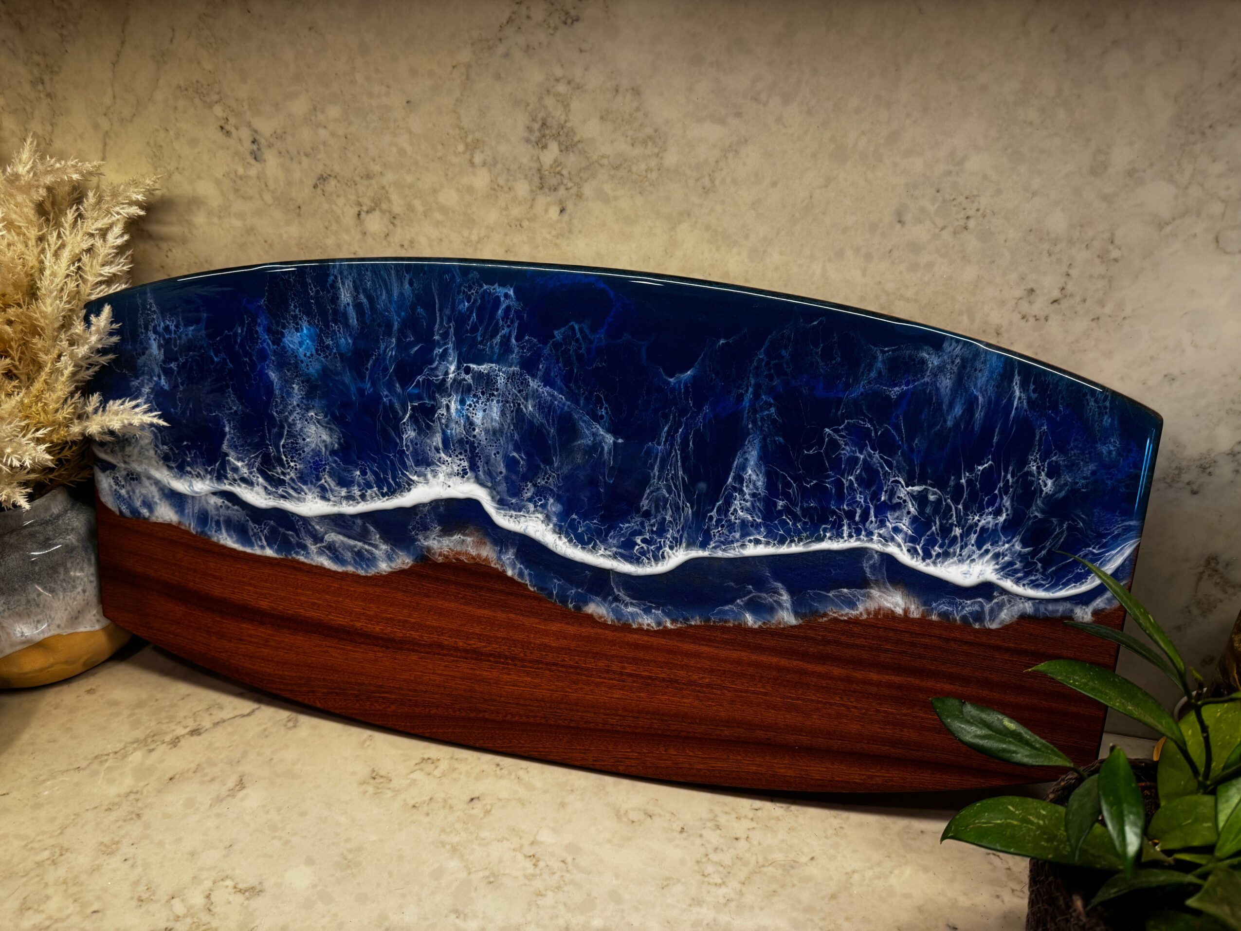 Decorative wooden bowl with blue and white marbled interior, placed on a beige surface with plants nearby.