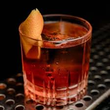 A glass of amber-colored drink with a lemon wedge on the rim, on a textured surface.