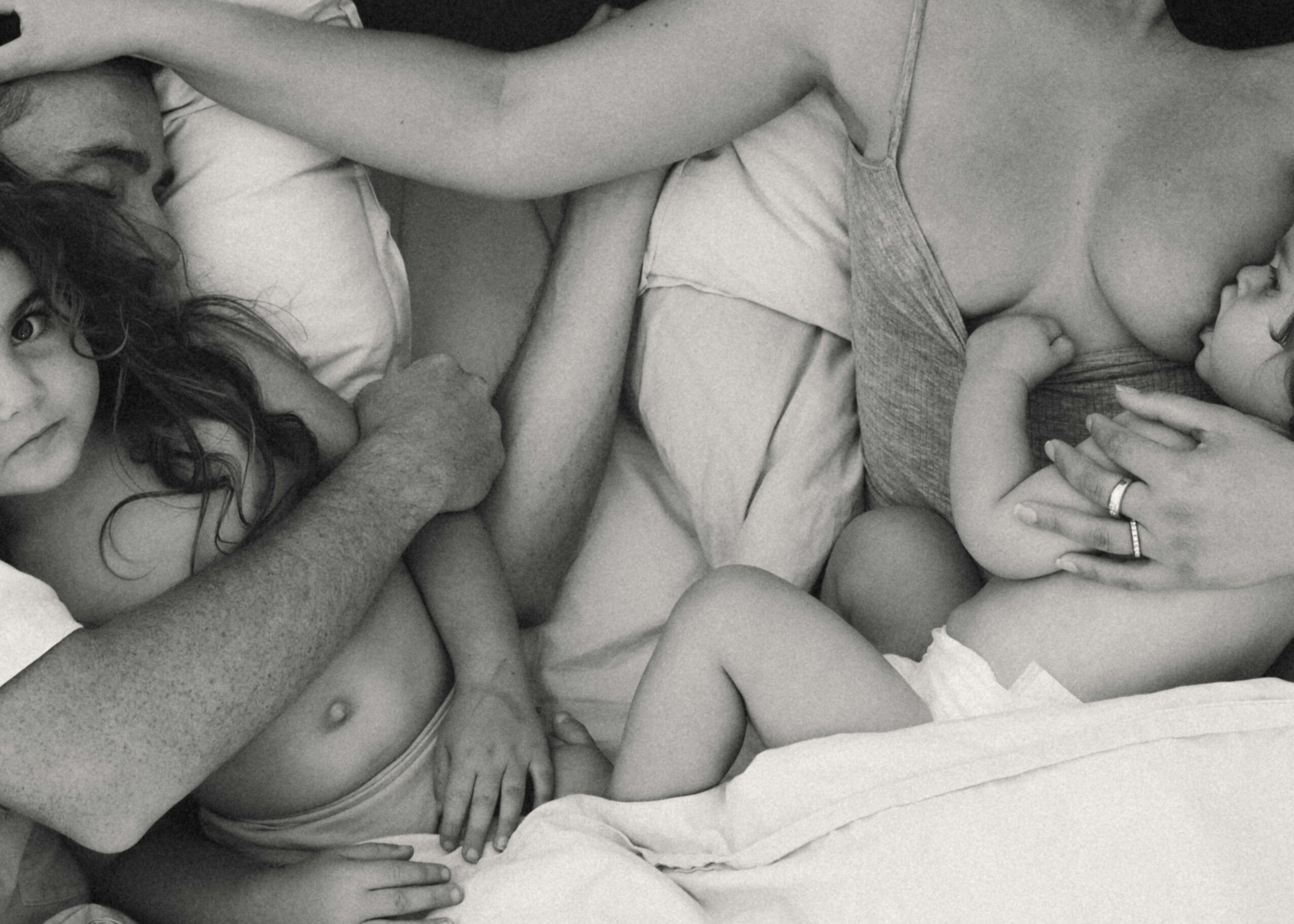 Two children and two adults lying on a bed, with one adult reaching towards a child, all in grayscale.
