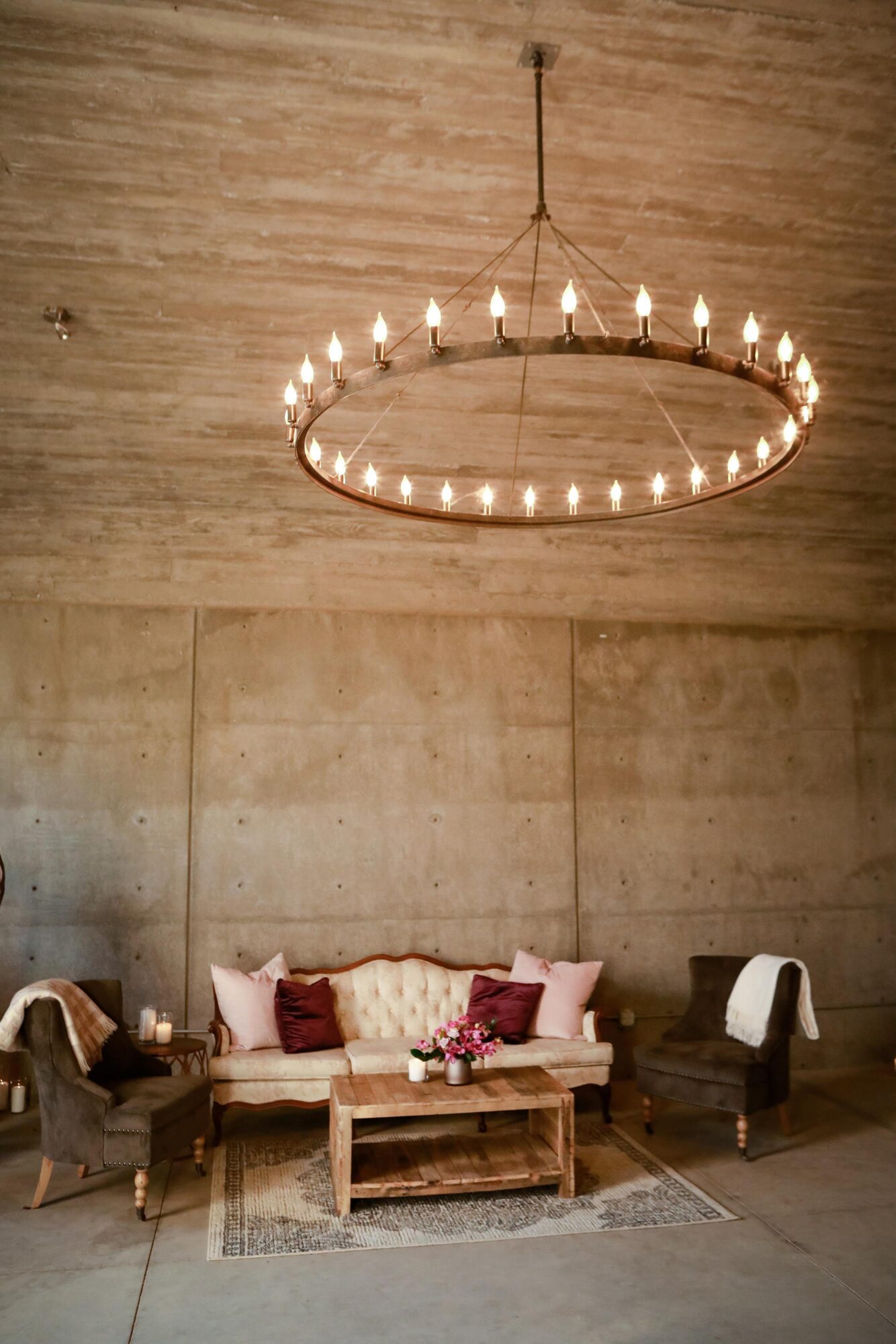 Chandelier hanging from ceiling above a seating area with sofa, armchairs, and a coffee table in a room with concrete walls.