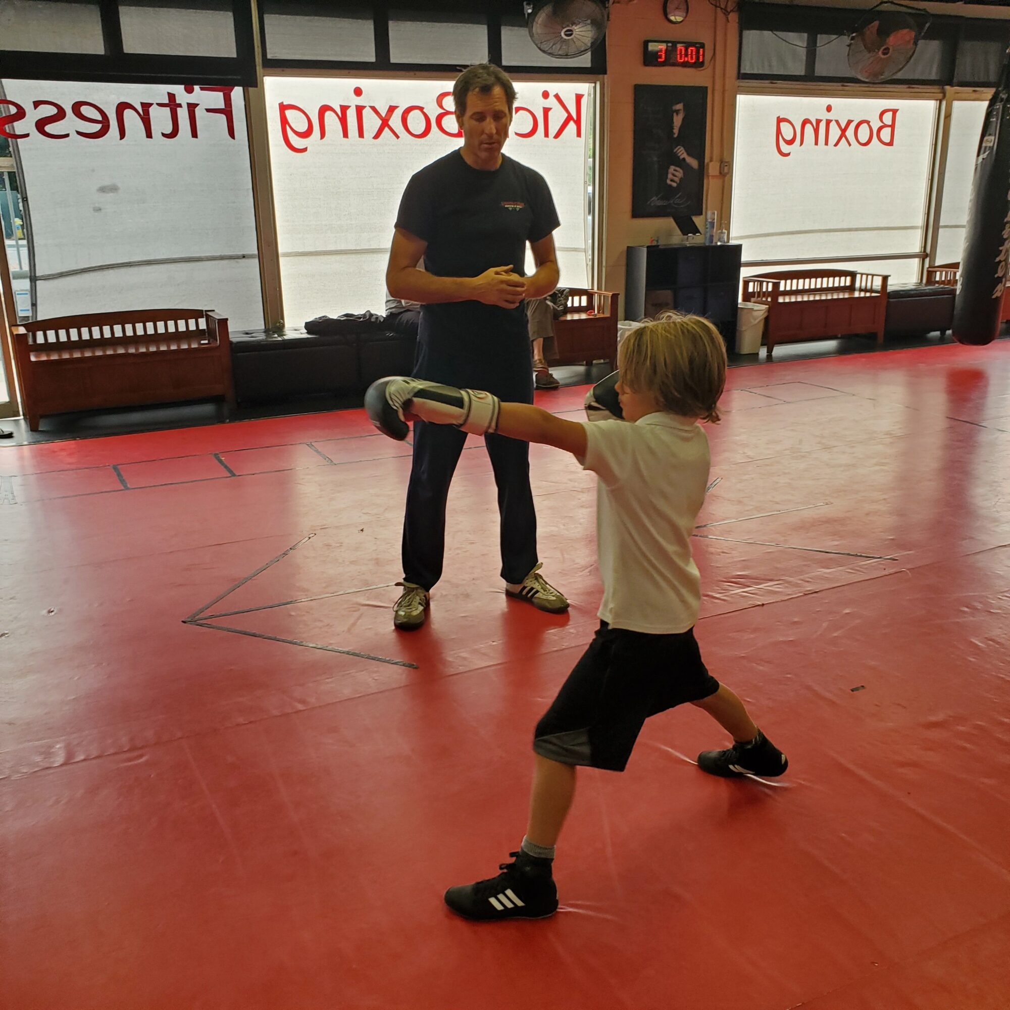 Young boy practicing a punch with a padded target held by an instructor in a martial arts studio.