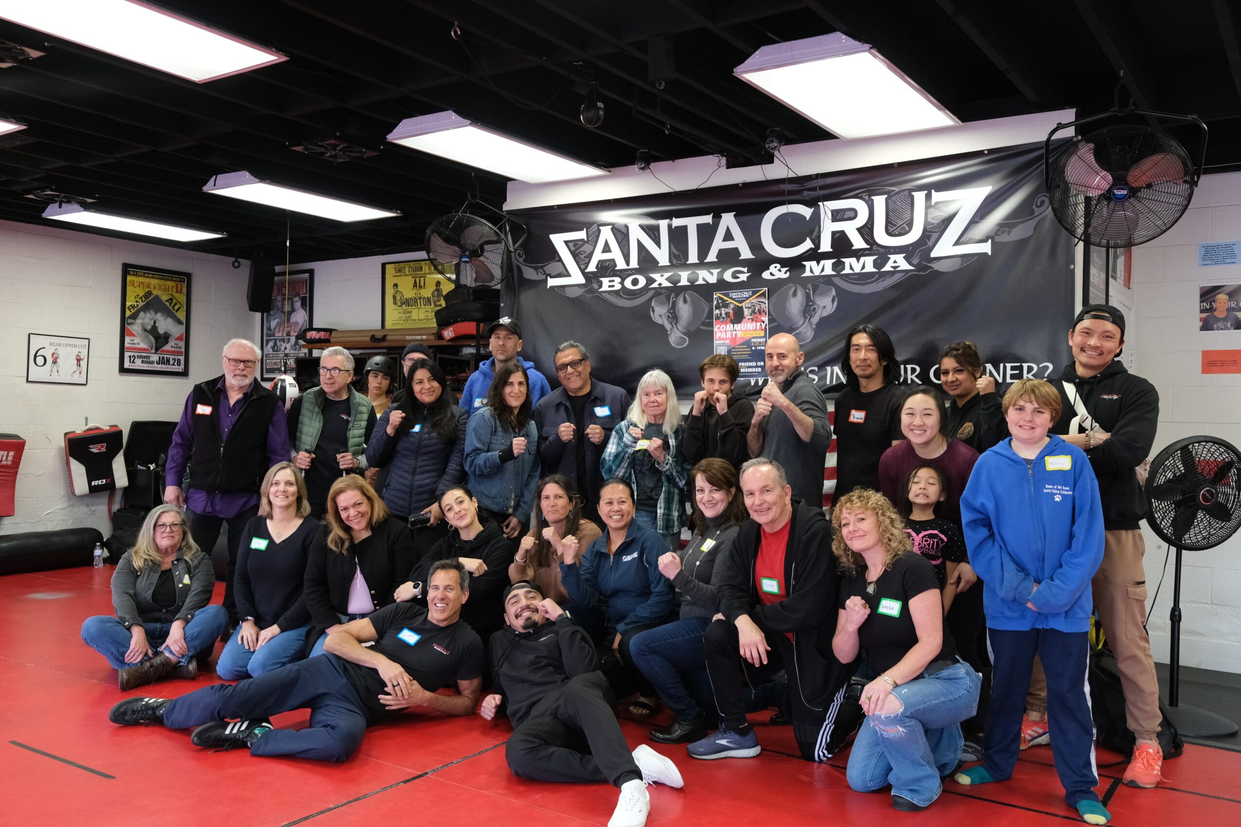 Group of people posing in a gym with a Santa Cruz Boxing & MMA banner behind them.