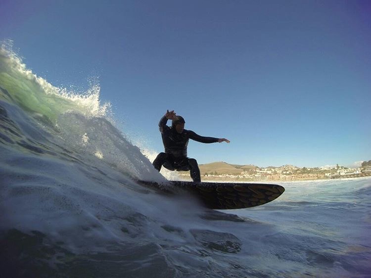 Person surfing on a wave with a clear sky and distant shoreline in background.