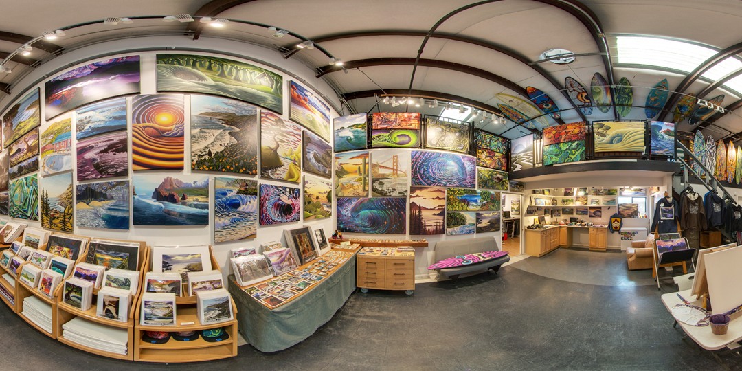 Gallery wall with landscape paintings, postcards, and merchandise in a store, curved ceiling, wooden furniture, and display tables.
