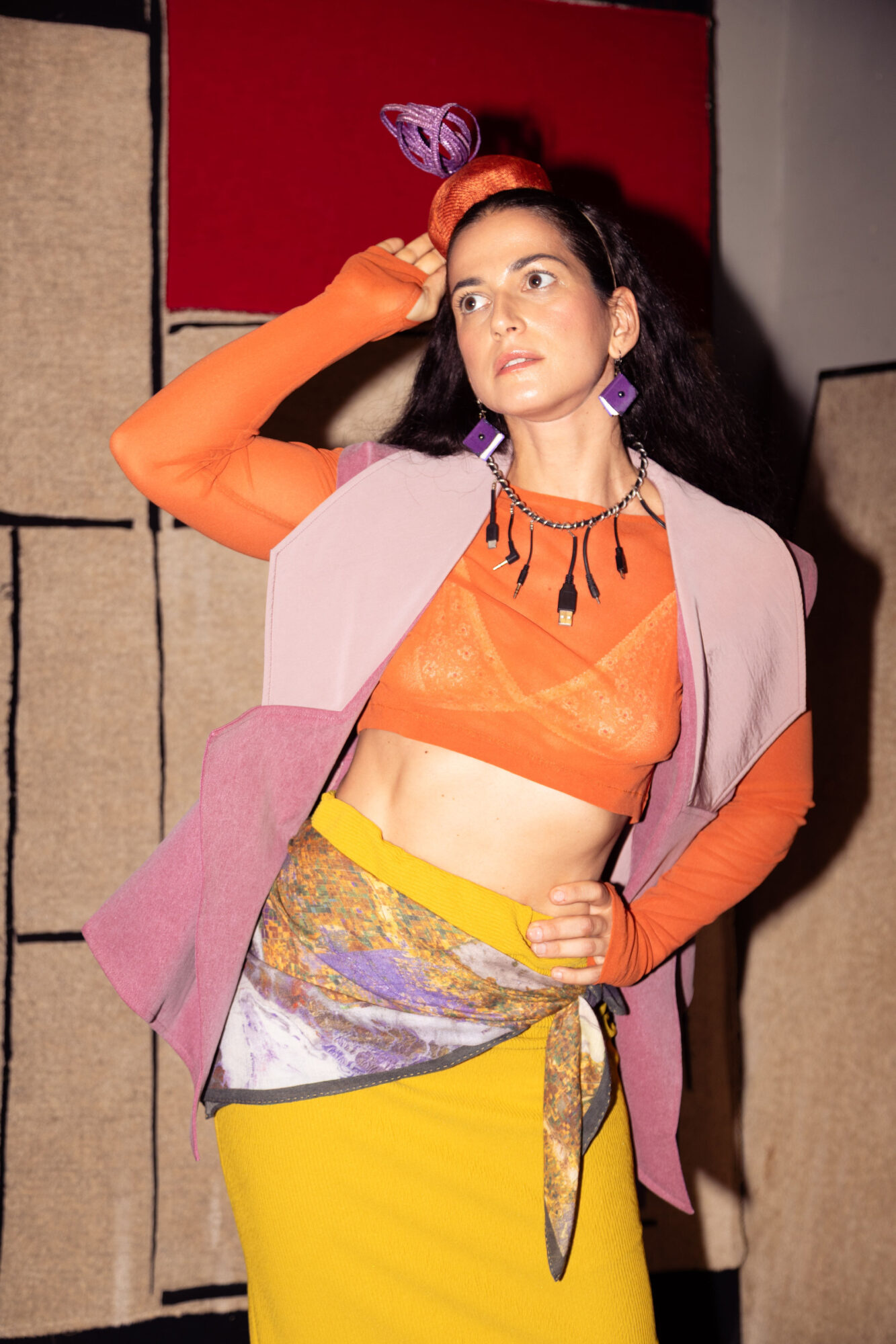 Young woman with colorful clothing and accessories, standing indoors with a neutral background.