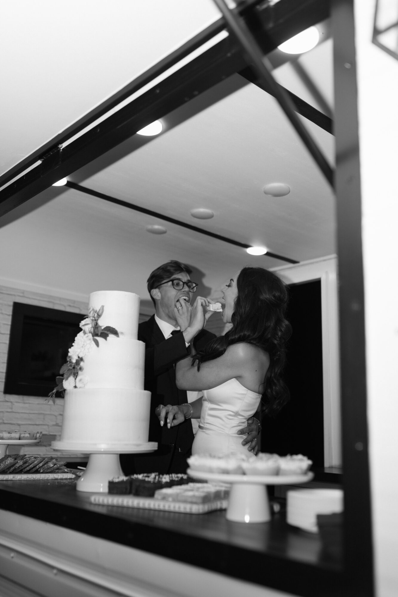 Two people dancing at a celebration, with a cake in the foreground and a ceiling with recessed lights above.